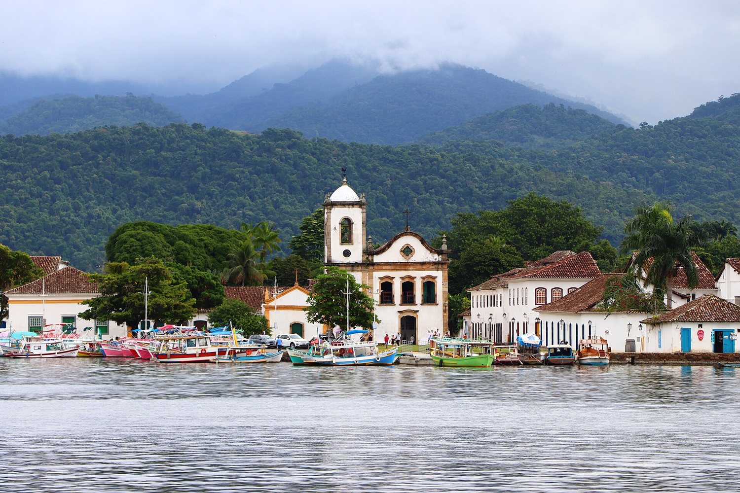 Paraty seen from its bay — the white Santa Rita church, fishing boats, and the forested Serra do Mar behind.
