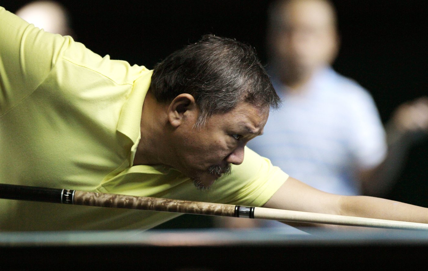 Efren Reyes in a yellow polo shirt leans low over his cue, sighting down the shaft with deep focus during a match.